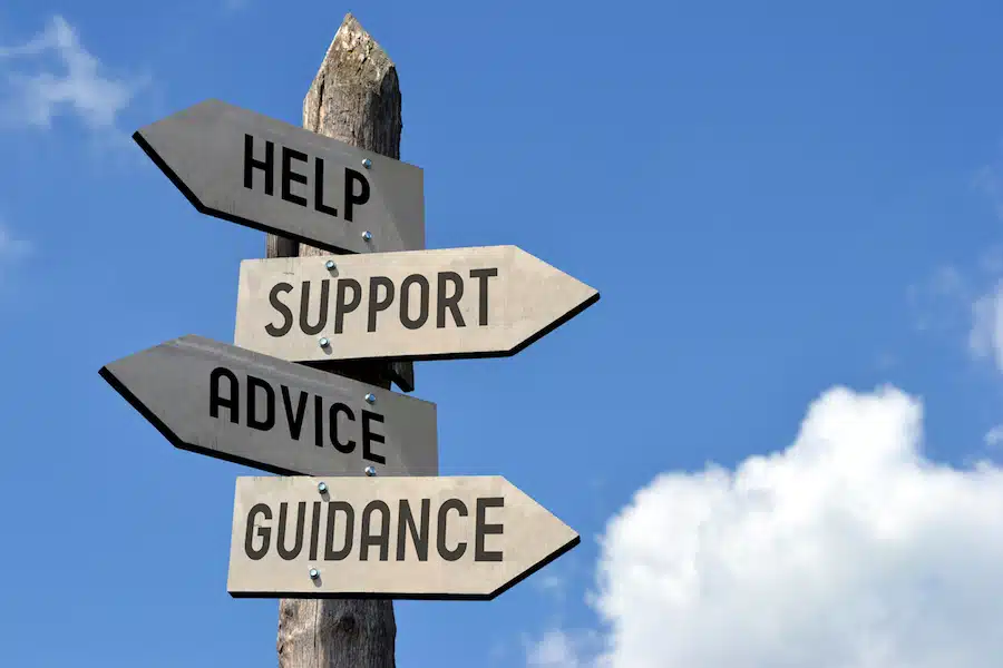 Wooden signpost with "help, support, advice, guidance" arrows against blue sky.