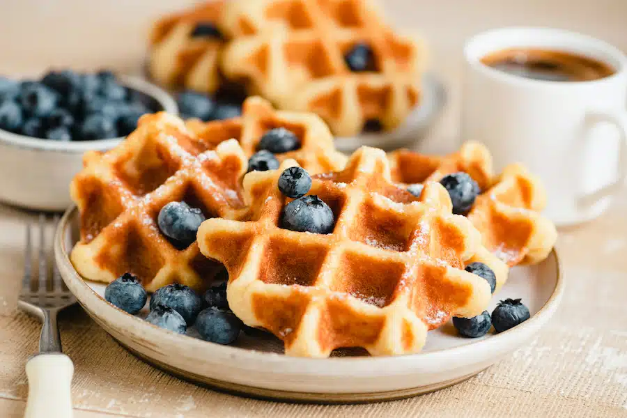 Belgian waffles with blueberries and cup of coffee on wooden table. Sweet breakfast food