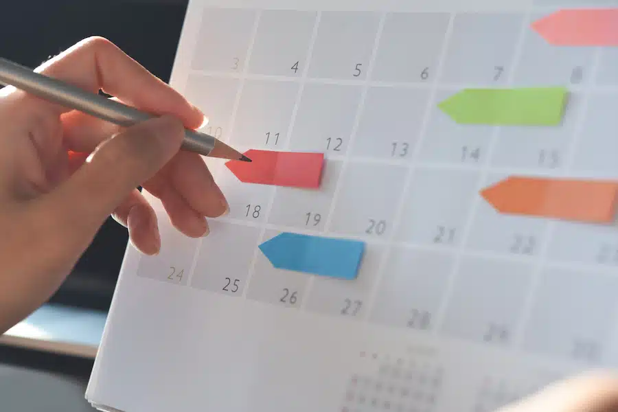 Event planner timetable agenda plan on organize schedule event. Business woman checking planner on mobile phone and taking note on calendar desk on office table. Calendar event plan, work planning, project management concept