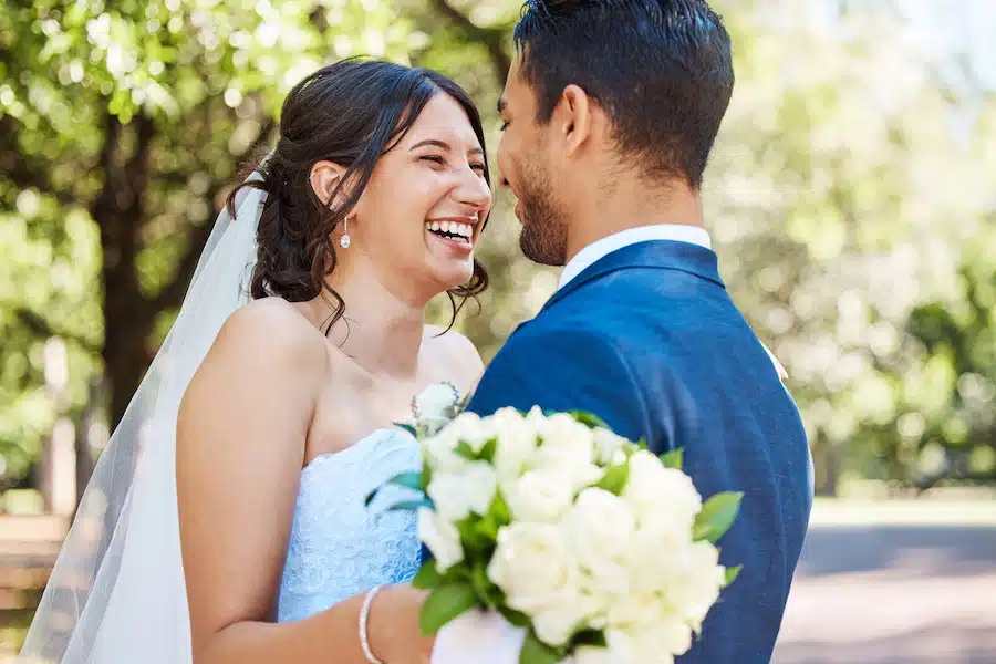 Happy young couple on their wedding day at their event venue. Husband and wife standing face to face laughing and enjoying romantic moments in nature