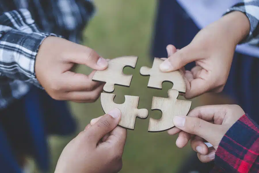 people helping in assembling puzzle, cooperation in decision making, team support in solving problems and corporate group teamwork concept, close up view of hands connecting pieces