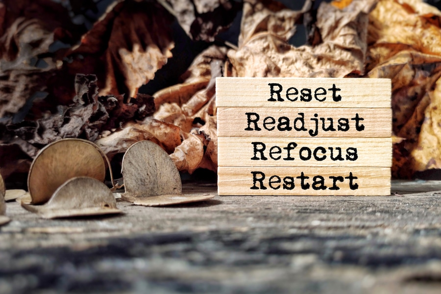 "Reset", "Readjust", "Refocus", "Restart" written on stacked blocks in front of a leafy background.