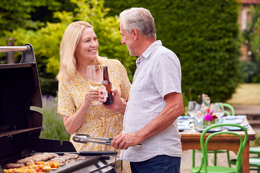 Senior Couple Cooking Outdoor Barbeque And Drinking Wine And Beer