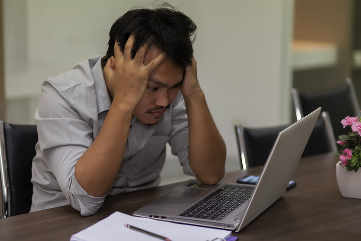 Asian business man feeling stressed due to the large volume of spam looking at his laptop. 