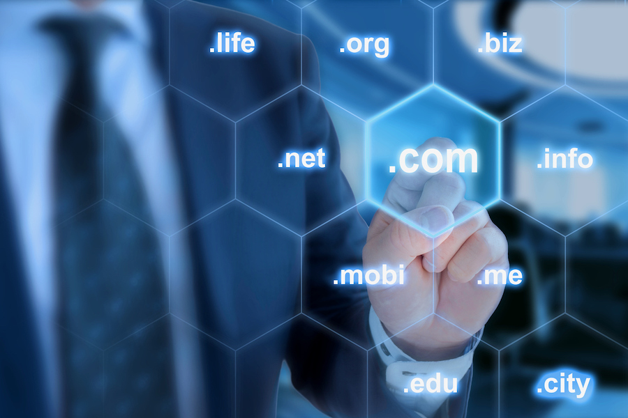Businessman in blue touching the domain ending com on a hexagon grid in front of office background