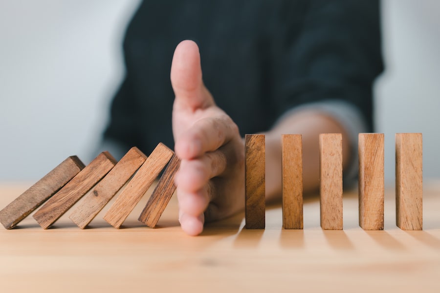 Hand stopping the wooden block domino effect of a business crisis or risk protection concept, prevention, and development to stability