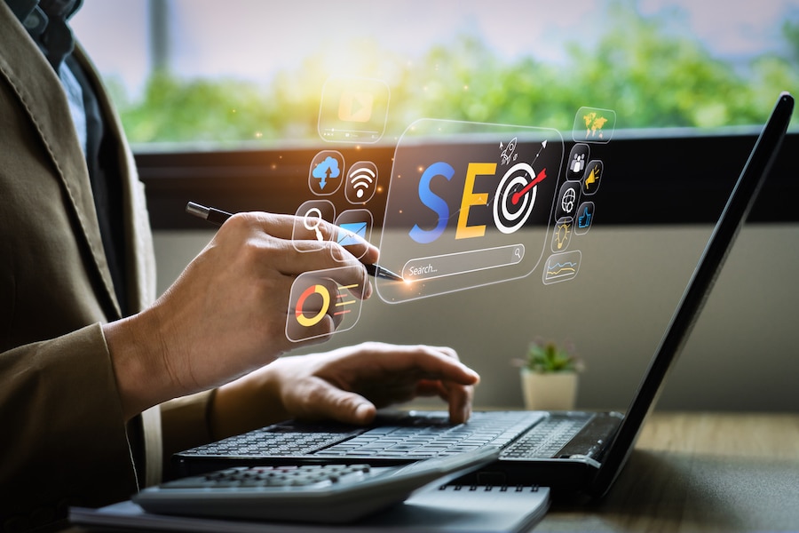 Business man using a pen to touch a virtual image of SEO, Analytics, and Wifi concept in front of a a laptop