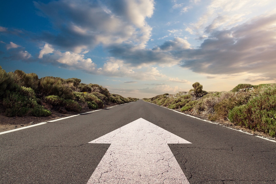 Blue sky with clouds and country road with white arrow pointing forward