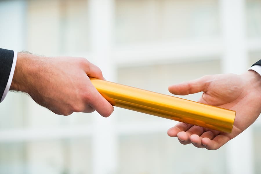 Cropped hand of businessman giving golden relay baton to the next business owner