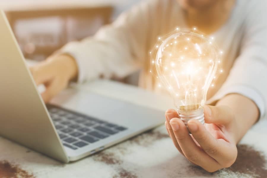 Woman hand holding light bulb and using laptop on wooden desk. Concept new idea with innovation and creativity.