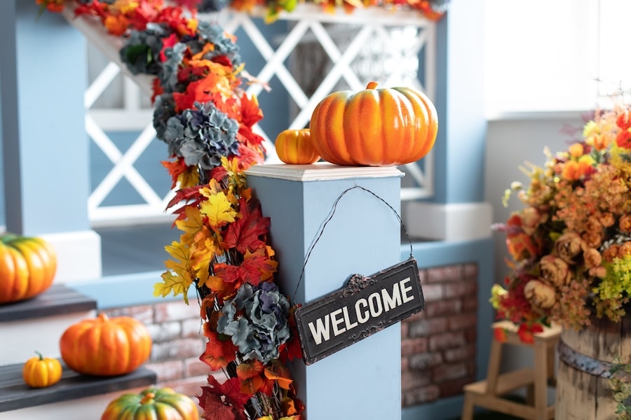 House decorated for Halloween holiday. Different colored pumpkins in front door On Wooden Steps. Porch of yard decorated with orange pumpkins in autumn. Thanksgiving. Halloween outside.