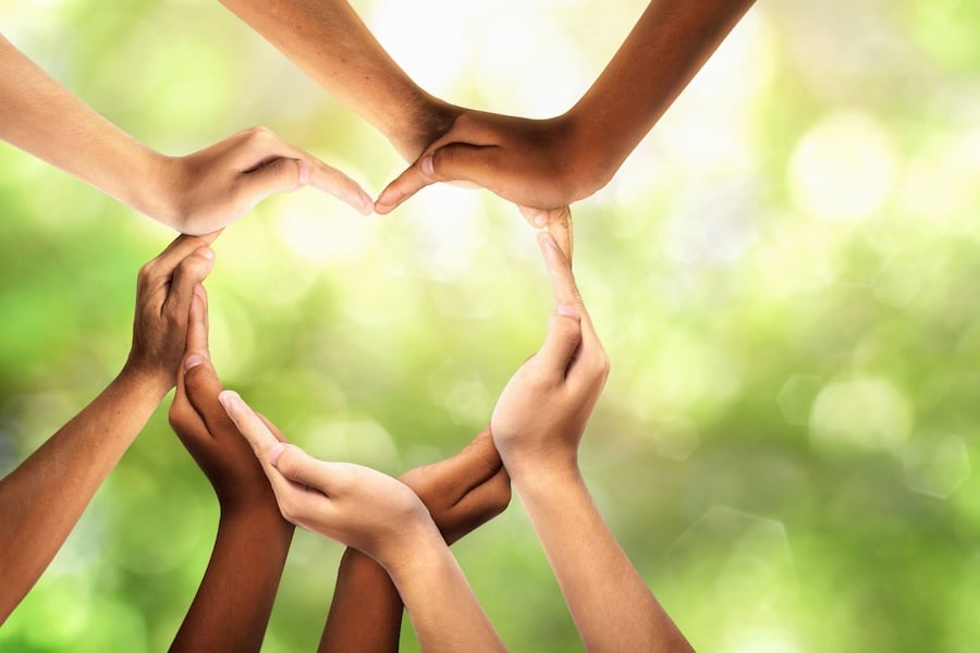 Group of people connected together as a supportive symbol that represents a sense of and togetherness. Symbol and heart-shape created from hands.