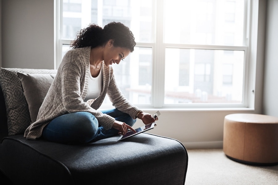 Shot of a cheerful young woman relaxing on a chair while  doing online shopping on a digital tablet at home