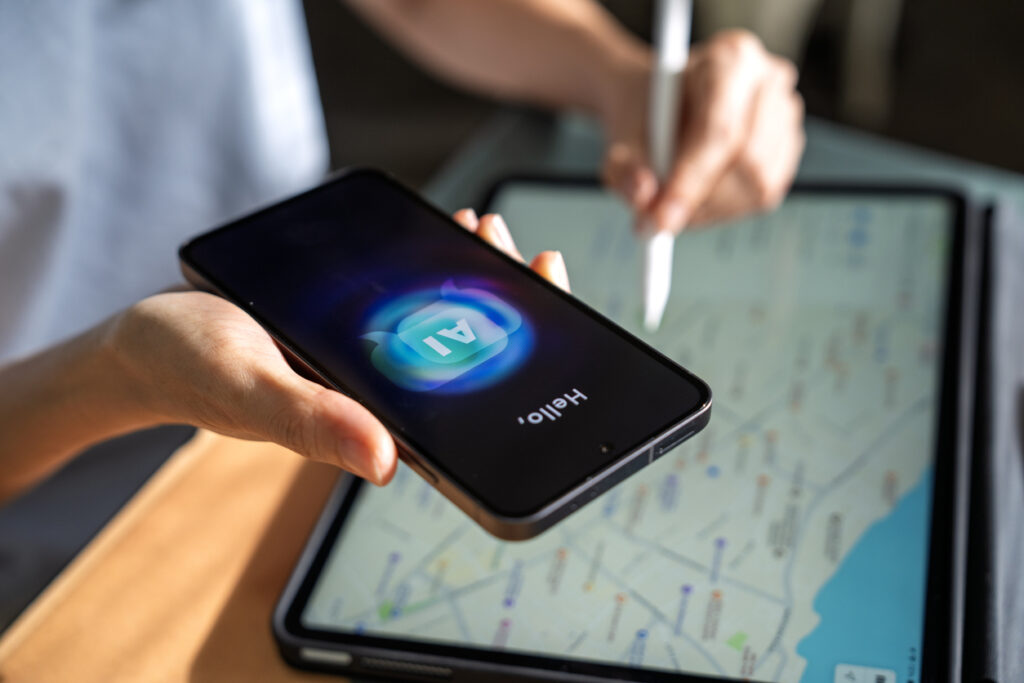 Close-up of a person using a smartphone with an AI chatbot interface while planning a trip with a digital map on a tablet. AI Search Optimization for Hotels is more important than ever